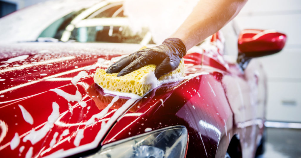 Worker washing red car with sponge on a car wash
