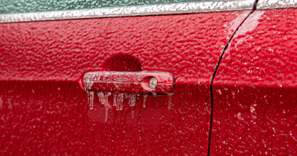 Closeup of car door handle and lock covered in ice during winter storm. Concept of winter driving preparedness and safety
