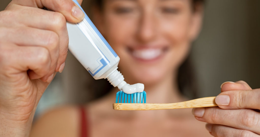 Close up of woman with tooth brush applying paste in bathroom. Closeup of girl hands squeezing toothpaste on ecological wooden brush. Smiling woman applying toothpaste on eco friendly toothbrush.
