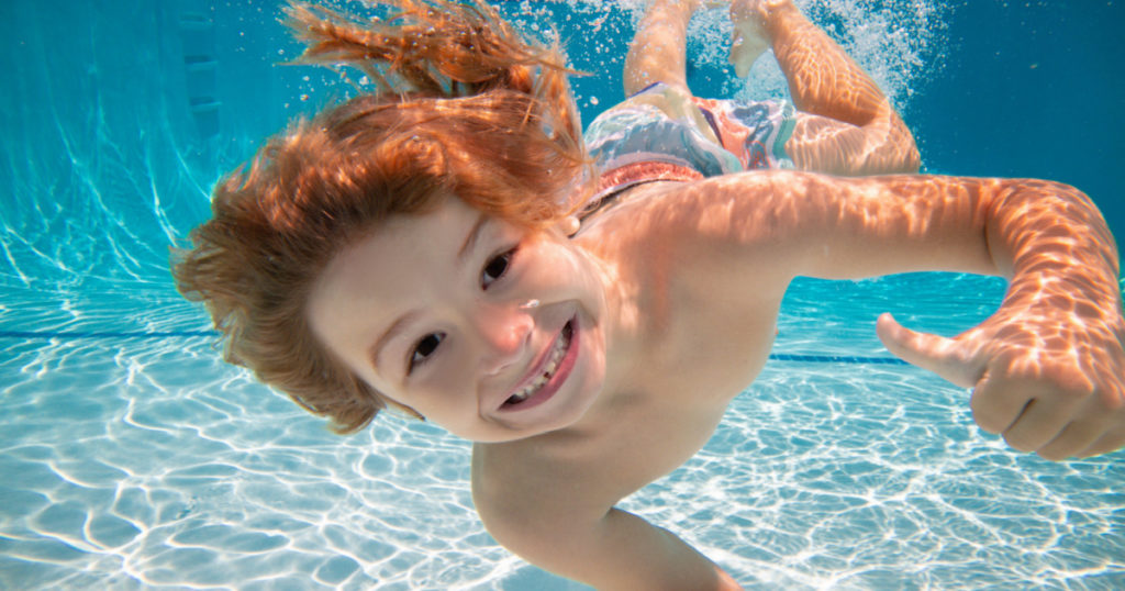 Happy kid boy swim and dive underwater, kid with fun in pool under water. Active healthy lifestyle, water sport activity and swimming lessons on summer vacation with child.
