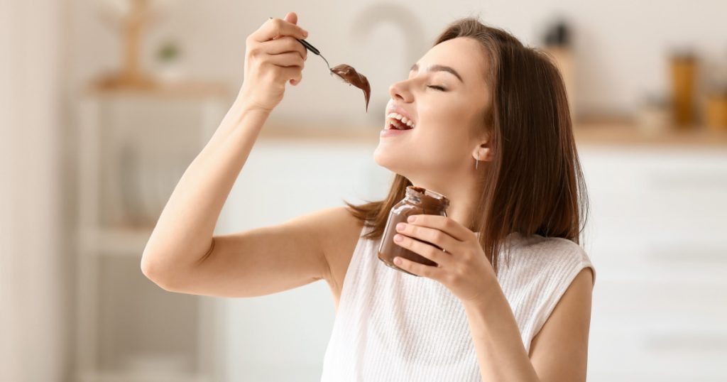 Beautiful young woman eating tasty chocolate paste at home
