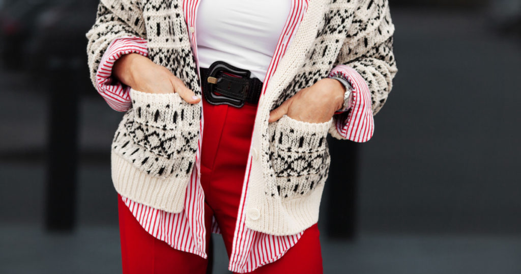 Street style details. Close up hands in pockets of stylish woman. Fashion blogger wearing sweater, shirt, belt and pants. Autumn or spring street fashion trend
