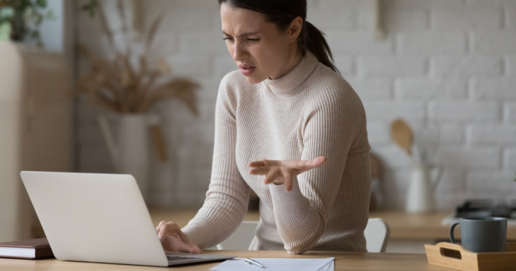 Irritated woman sit at table staring at laptop screen feels angry and confused having problems with broken computer, reading message with bad news in email, lost information, apps malfunction concept
