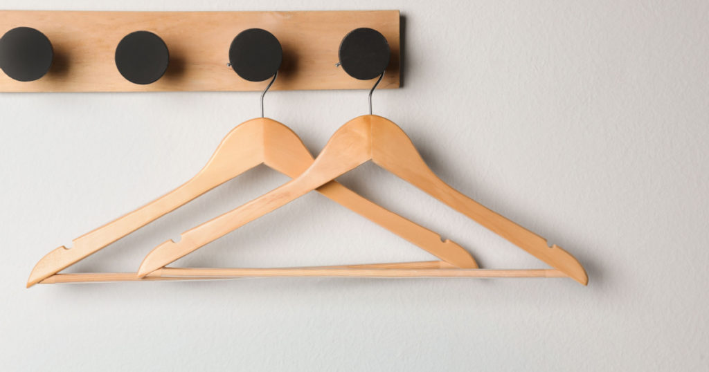 Rack with empty wooden clothes hangers on white wall

