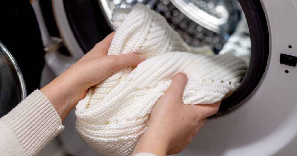 Woman putting white clothes into the drum of a washing machine, front view. Washing dirty clothes in the washer
