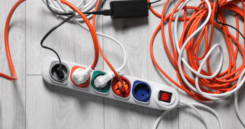 Power strip with different electrical plugs on white laminated floor, flat lay
