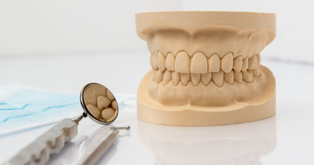 Dental mold showing the teeth of the upper and lower jaw with dental tools and a face mask on a wooden table in a dental care and examination concept
