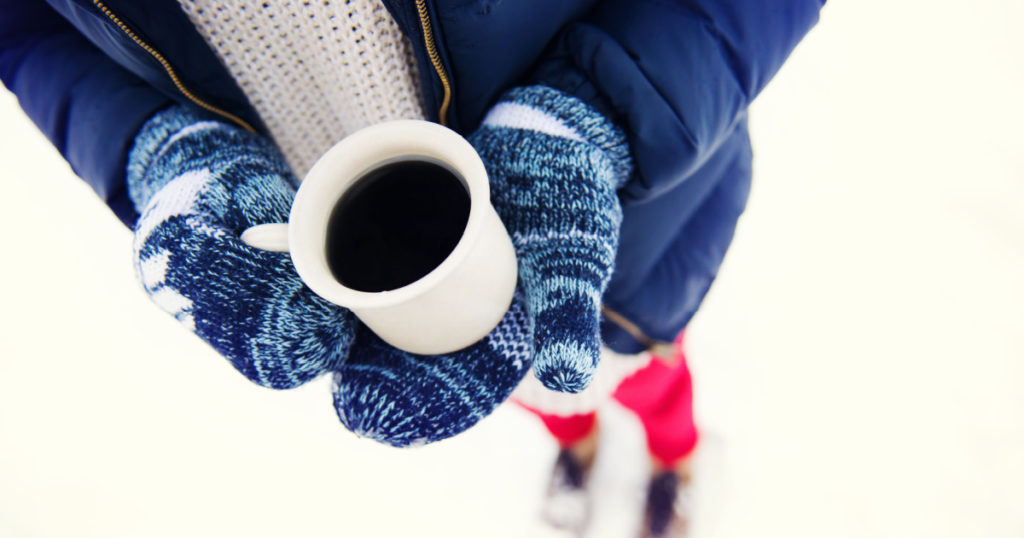 Hands of young woman holding a cup of coffee outside in snow
