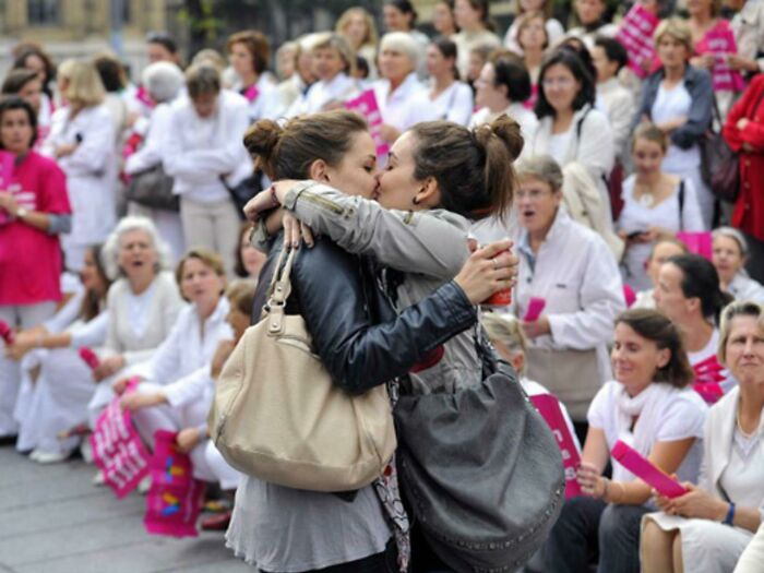 Two young women sharing a kiss in the presence of an anti-gay protest