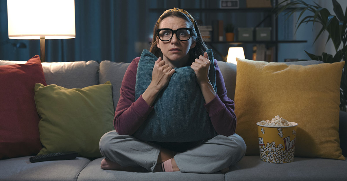 woman sitting on couch holding pillow in suspense. Scary movie concept