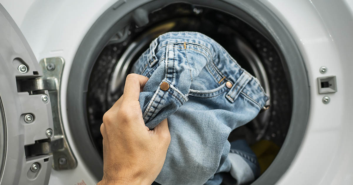 Front load laundry machine with hand placing jeans into it