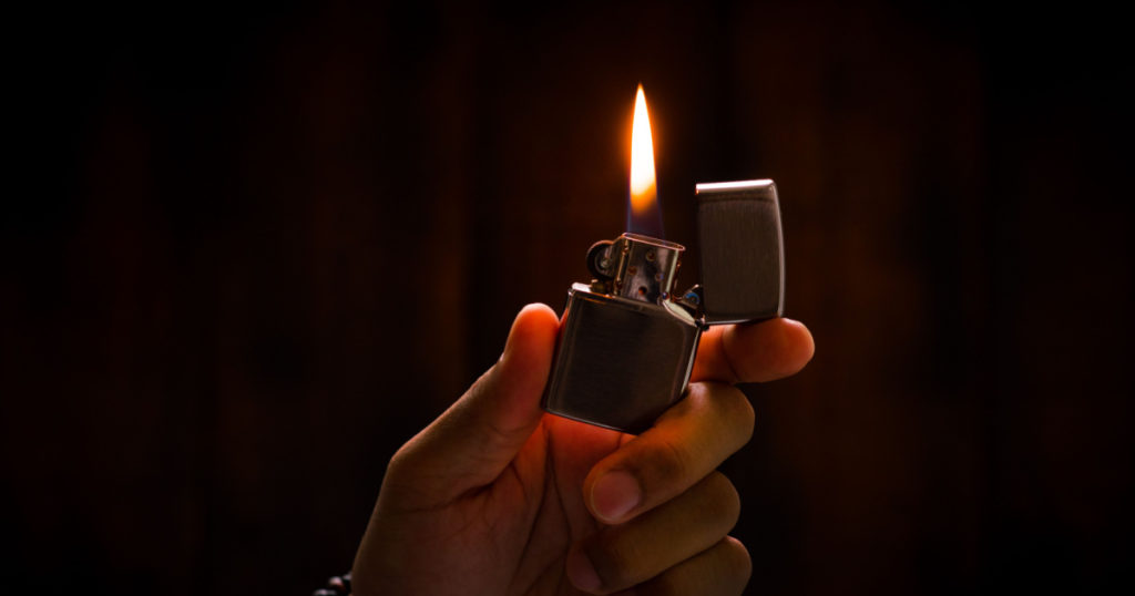 The man holding Brushed chrome lighter with windproof in the dark.
