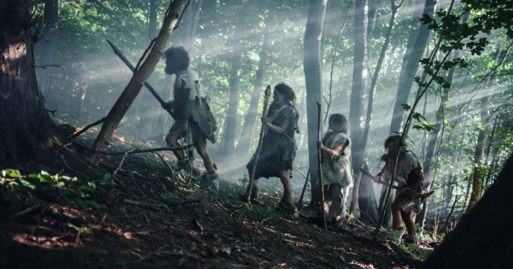 Tribe of Hunter-Gatherers Wearing Animal Skin Holding Stone Tipped Tools, Explore Prehistoric Forest in a Hunt for Animal Prey. Neanderthal Family Hunting in the Jungle or Migrating for Better Land
