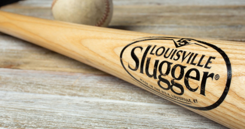 Los Angeles, California, United States - 02-25-2020: A closeup view of a Louisville Slugger wooden bat with a weathered baseball on a wooden surface.
