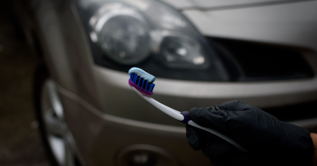 Technician with holding toothbrush and toothpaste to shine and brighten the headlights of the car. Topical car wash and care. car care. headlight polishing and care concept..
