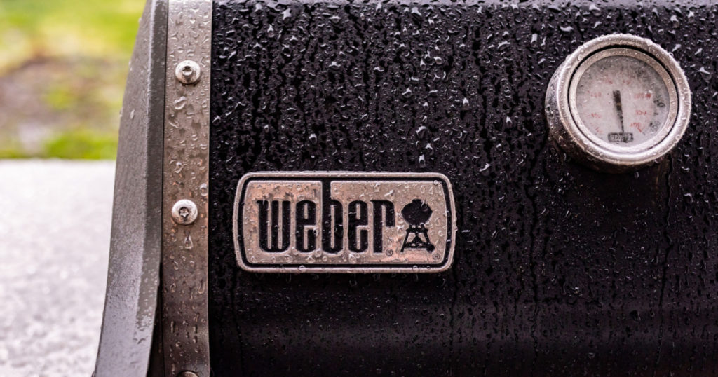 Hillsboro, Oregon / USA - 24 May 2020: Up close photo of a logo of Weber company of a top of a gas grill covered in raindrops
