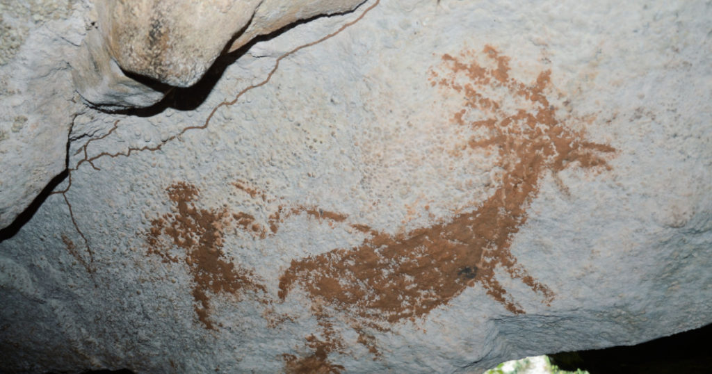 Photograph of an ancient painting on a cave wall depicting a person hunting a horned deer. Found in Muna, Southeast Sulawesi.
