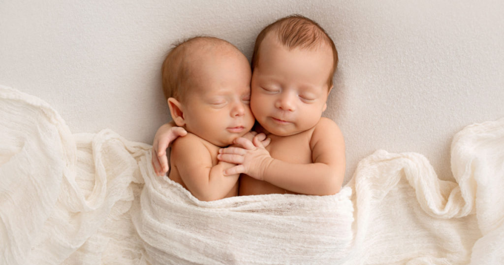 Tiny newborn twins boys in white cocoons on a white background. A newborn twin sleeps next to his brother. Newborn two twins boys hugging each other.Professional studio photography
