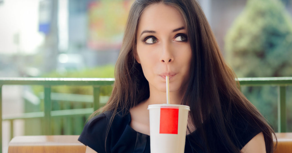 Young Woman Having a Summer Refreshing Drink Outside - Portrait of a funny girl drinking trough a straw
