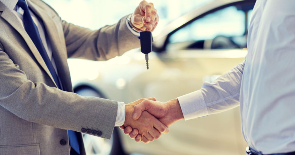 auto business, car sale, deal, gesture and people concept - close up of dealer giving key to new owner and shaking hands in auto show or salon
