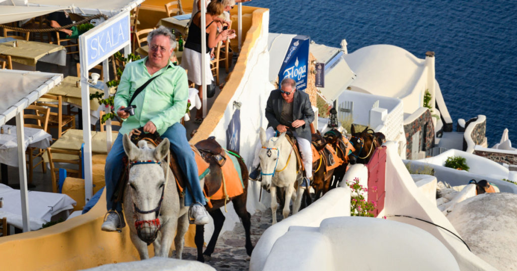SANTORINI, GREECE - SEPTEMBER 22, 2014 - Some tourists go up the stairs from the port of Oia to the city center by donkey.
