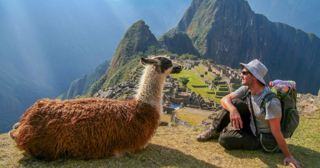 Tourist and llama sitting in front of Machu Picchu, Peru
