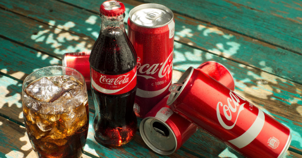 MINSK, BELARUS-AUGUST 26, 2016: Glass of Coca-Cola with ice, can and bottle of Coca-Cola on wooden background. Coca-Cola is a carbonated soft drink sold in stores, throughout the world.
