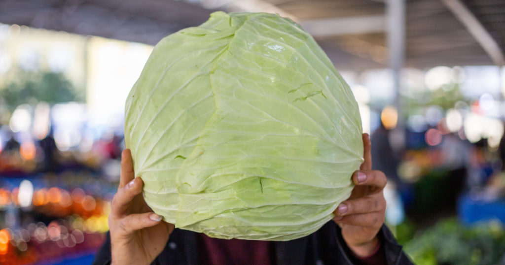 Man holding a giant cabbage larger than his head at a farmer's market
