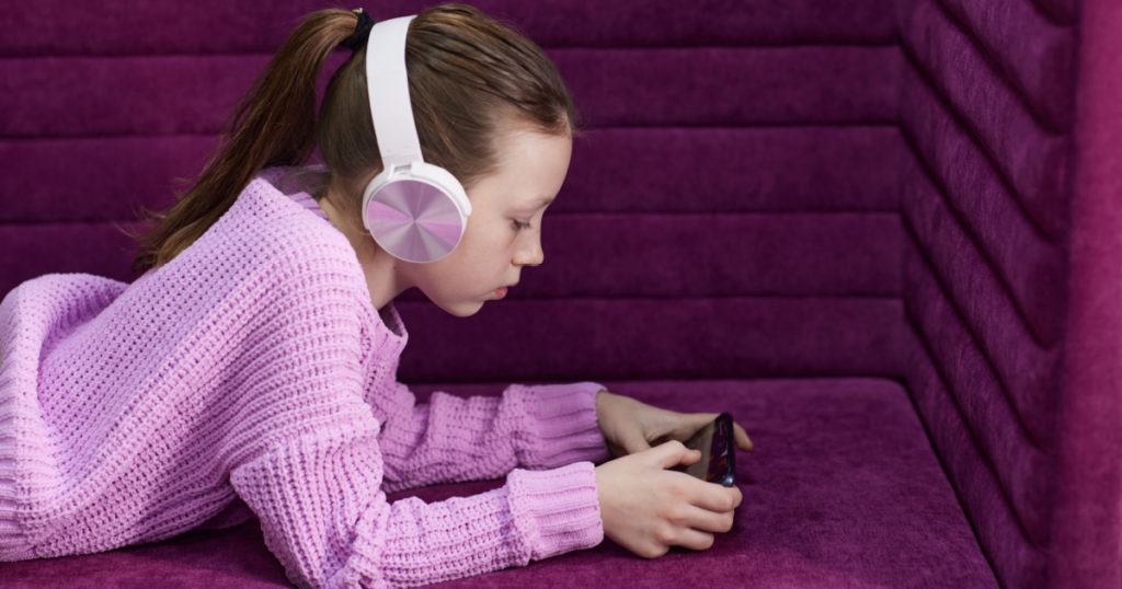 little girl plays in a children's room with headphones and a smartphone. using a mobile phone with a headset and watching videos at home. Girl's homework using the app
