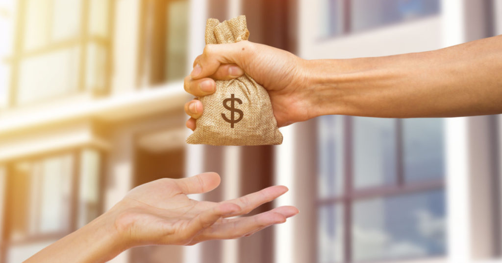 A man hand holding a money giving to another person for buying real estate. Loans for real estate concept. Conceptual give money to someone else to exchange real estate.
