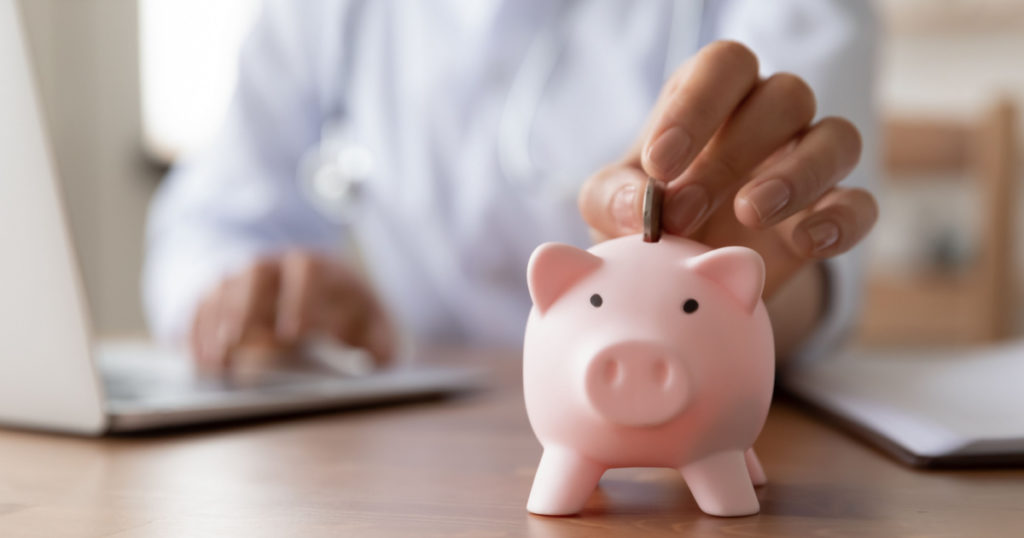 Crop close up of woman doctor hand put coin in piggybank, make monetary donation to clinic fund, female drop money contribution or volunteer charity in piggy bank for patient or hospital need care
