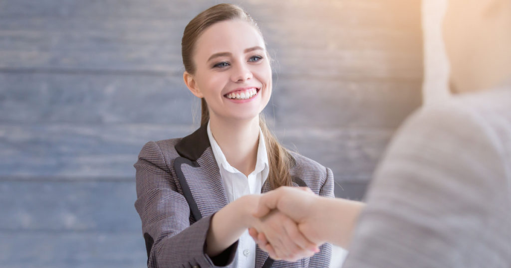 Young woman arriving for a job interview. Business people handshake in modern office. Greeting deal concept
