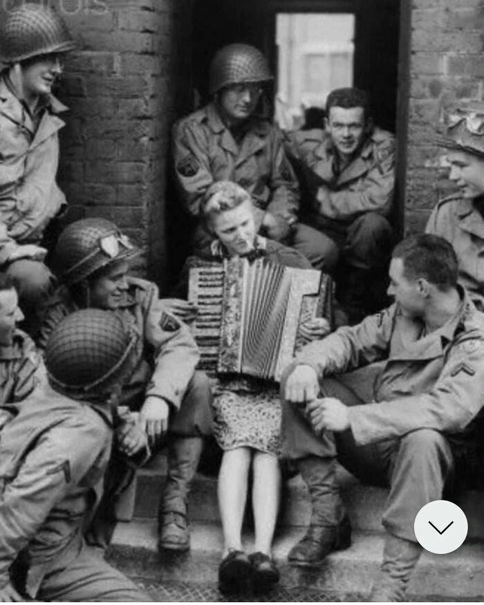 In a heartwarming scene from 1944 England, Mrs. Hale, the wife of a British soldier, shares a moment of camaraderie by playing the accordion outside her house for a group of American soldiers.