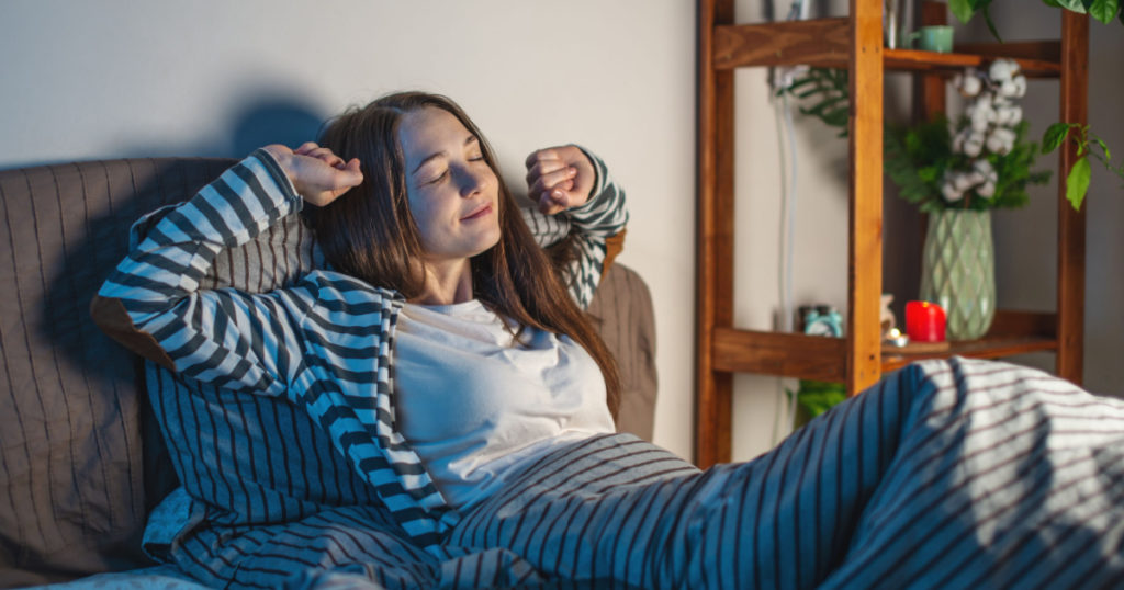 A young happy woman is lying in her cozy bed, stretching and getting ready for bed. Concept of bedtime pastime and rituals for a healthy and restful sleep.