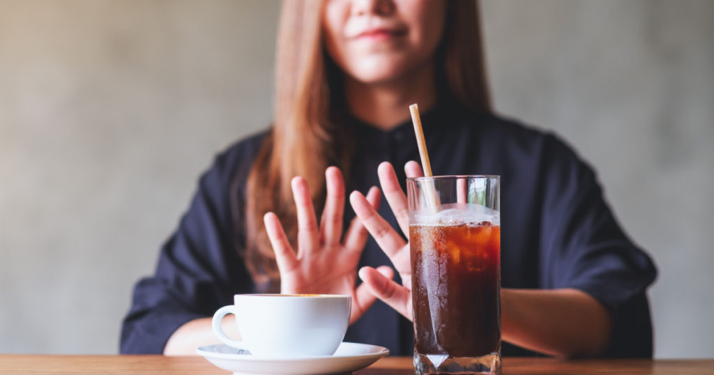 A young woman making hand sign to refuse iced coffee and hot coffee