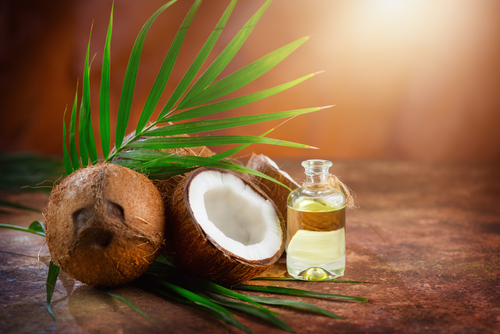 Coconut palm oil in a bottle with coconuts and green palm tree leaf on brown background. Coco nut closeup. Healthy Food, skin care concept. Vegan food. Skincare treatments. Aromatherapy.